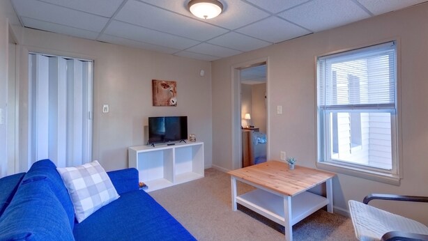 A living room with a blue sofa, a wooden coffee table, a TV on a white stand, and a window with blinds. - Candy Bar, Apt #8
One Bedroom with pull out (Hershey)