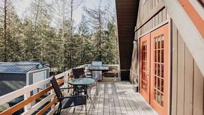 A wooden deck with a grill, table, and chairs, surrounded by trees.