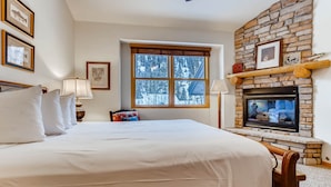 A bedroom with a large bed, a fireplace, and a window with a view of trees. - Premiere 2br Townhome - Shuttle To Slopes. Kids Ski Free! 2 Bedroom Condo by RedAwning (Keystone)