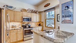 A modern kitchen with wooden cabinets, a stainless steel refrigerator, a microwave, an oven, and a granite countertop. - Premiere 2br Townhome - Shuttle To Slopes. Kids Ski Free! 2 Bedroom Condo by RedAwning (Keystone)