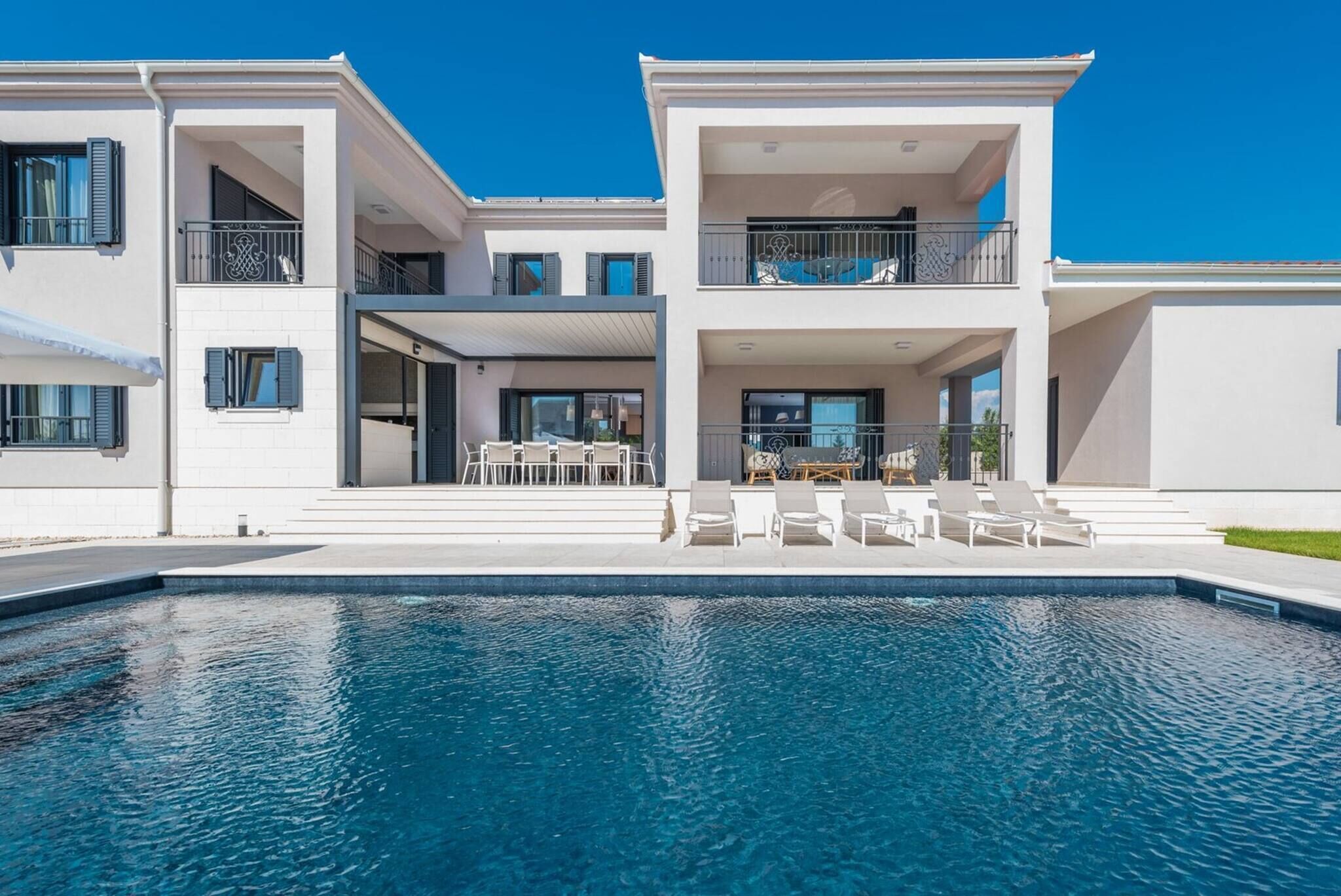 Un bâtiment moderne à deux étages, doté d’une piscine, d’un espace extérieur aménagé et de balcons.