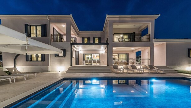 A modern two-story house with a swimming pool, outdoor seating, and a well-lit entrance.