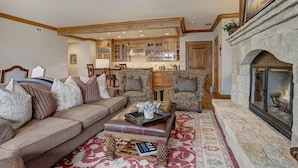 A cozy living room with a sofa, armchairs, a fireplace, and a kitchen in the background. - 4br Ski In/ski Out The Top Of Bachelor Gulch 4 Bedroom Condo by RedAwning (Avon)