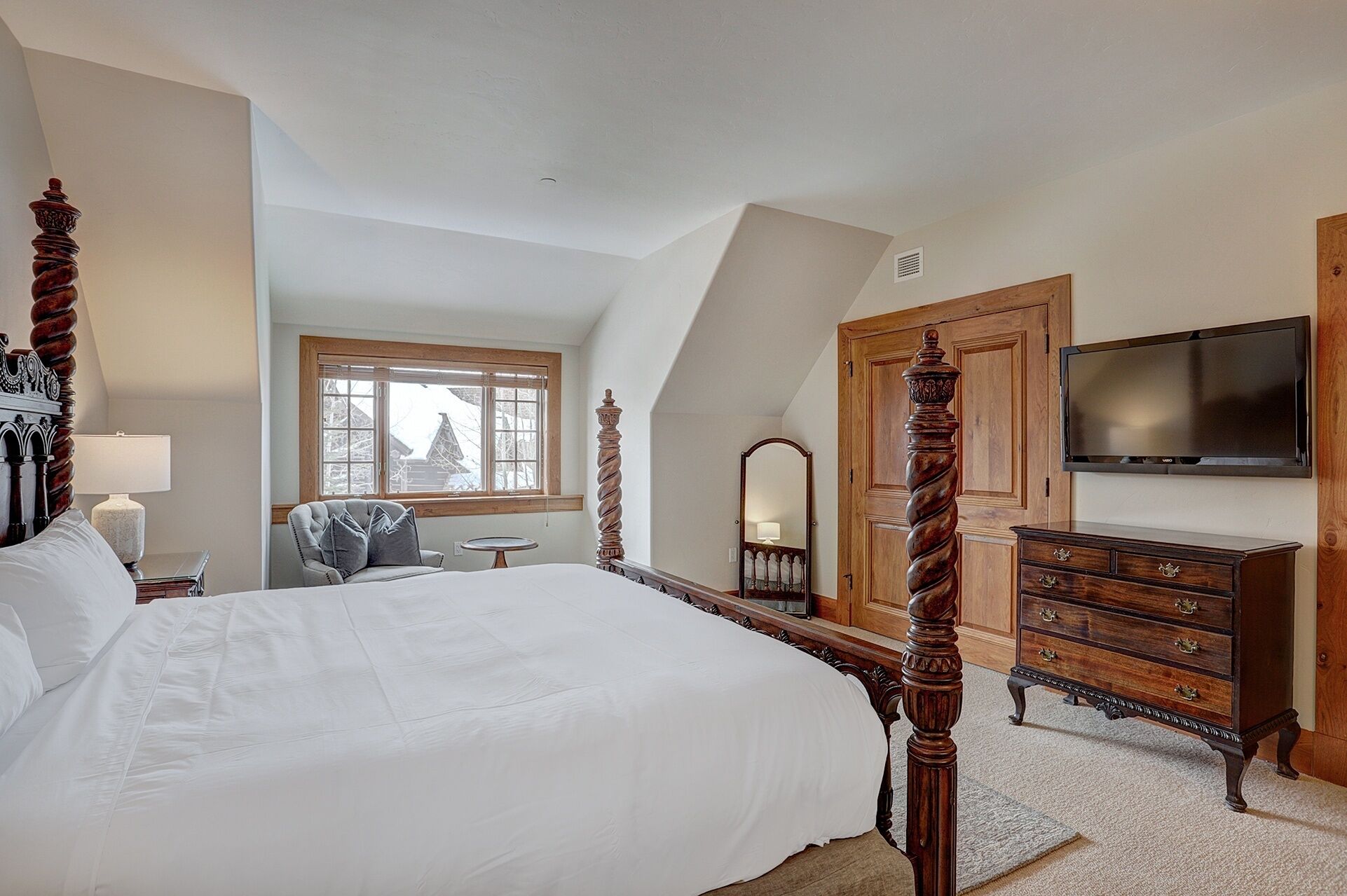 Ein Schlafzimmer mit Himmelbett, Schminktisch, Fernseher und Fenster mit Blick auf schneebedeckte Gebäude.