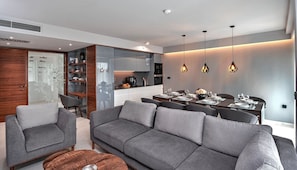 Uma sala de estar moderna com um sofá cinzento, uma mesa de centro e uma área de jantar com mesa posta para quatro pessoas.