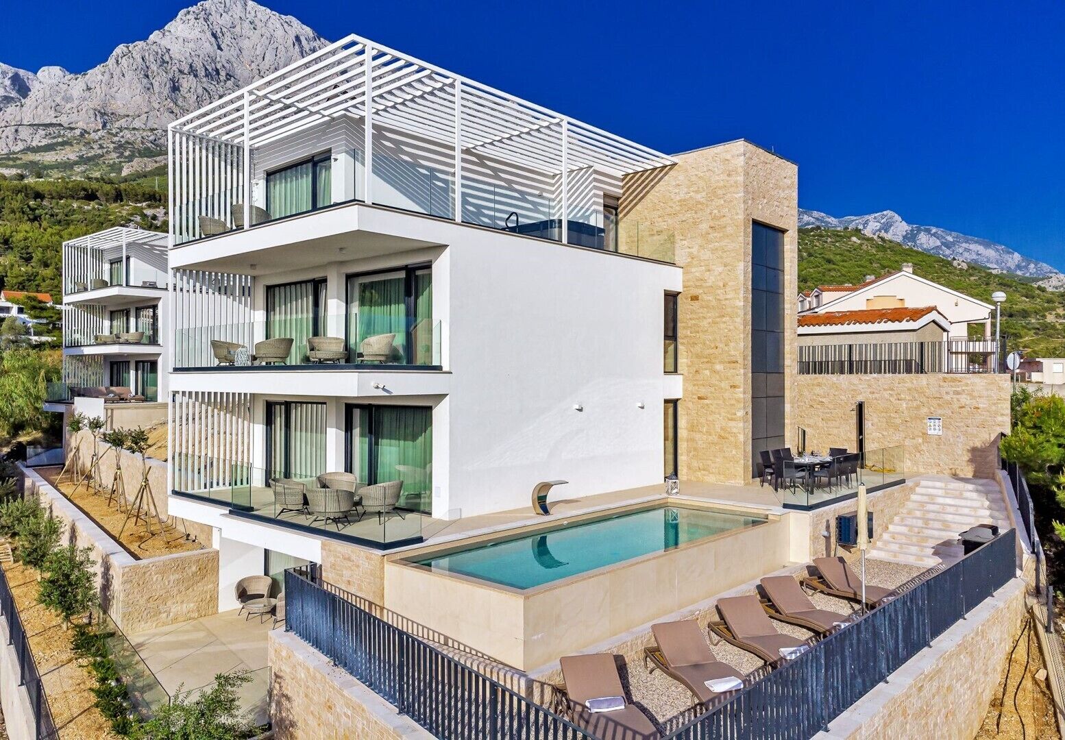 Un bâtiment moderne à deux étages doté d’une piscine, d’un espace extérieur aménagé et offrant une vue sur les montagnes.