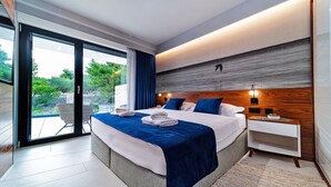 A modern bedroom with a large bed, a nightstand, and a view of the outdoors. - Luxury Villa Delight I – Promajna, Heated Pool (Promajna)