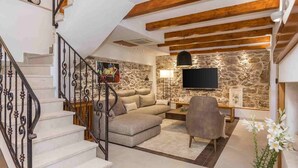 Un salon avec un mur en pierre, un canapé, un téléviseur, une lampe et un escalier.