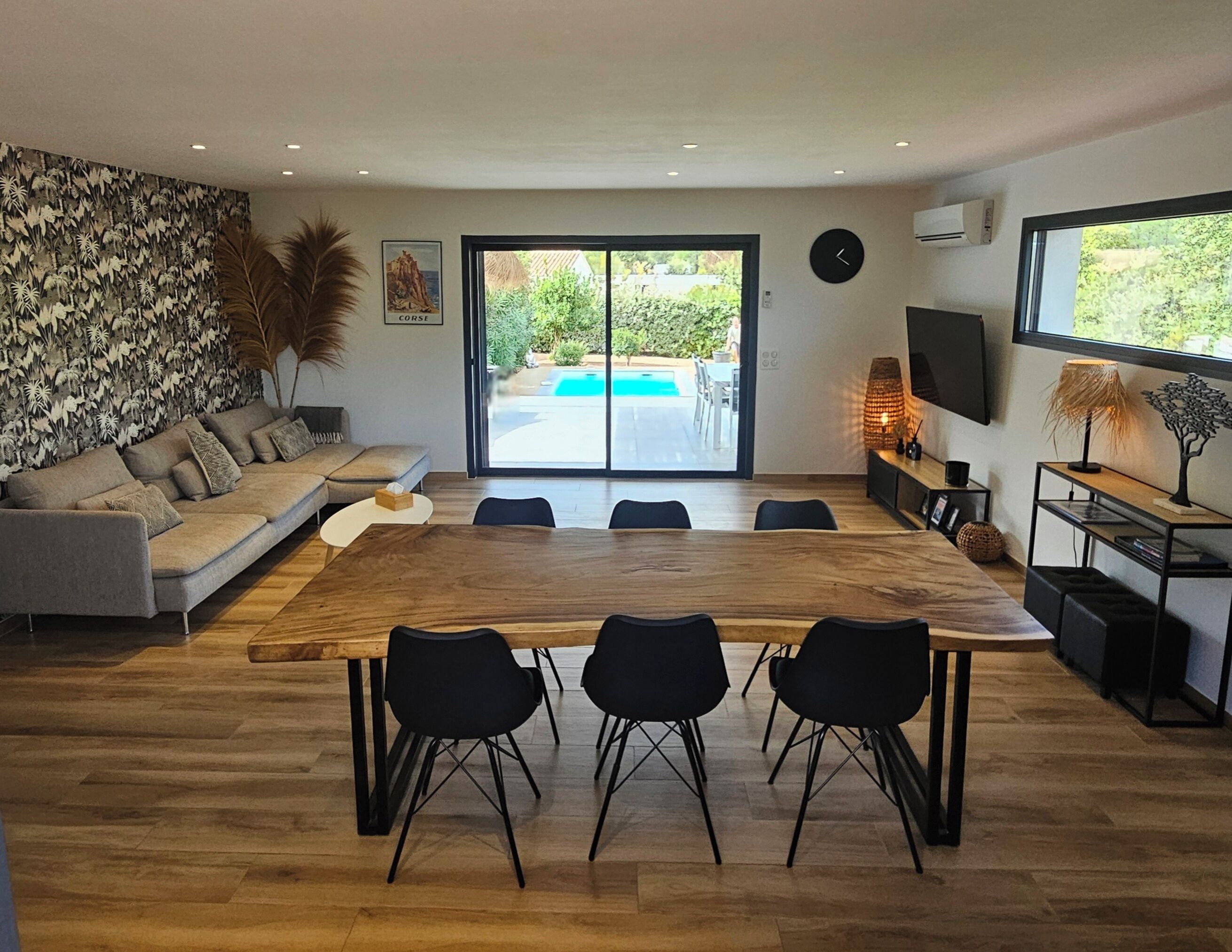 Un salon moderne avec une grande table à manger en bois, des chaises noires, un canapé gris et un mur décoratif.