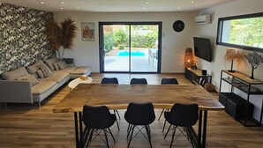 A modern living room with a large wooden dining table, black chairs, a grey sofa, and a decorative wall.