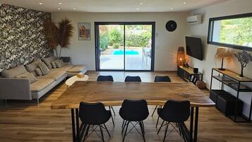 Un salon moderne avec une grande table à manger en bois, des chaises noires, un canapé gris et un mur décoratif.
