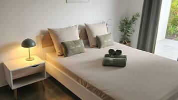 A modern bedroom with a bed, bedside tables, a lamp, a potted plant, and a painting on the wall.