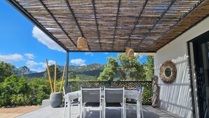 A covered patio with a table and chairs, a decorative wall, and a view of mountains.