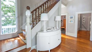A staircase with wooden balusters and a white railing, a white console table with lamps, and a wooden floor.