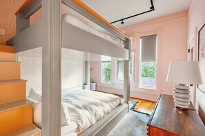 A bunk bed with a wooden headboard, a bedside table with a lamp, and a window with curtains.