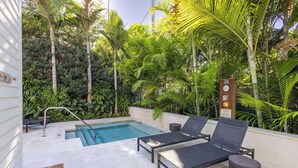 A poolside area with lounge chairs, a pool, and lush greenery.