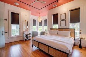 Quarto com uma cama grande, um candelabro e vista para o verde pelas janelas.