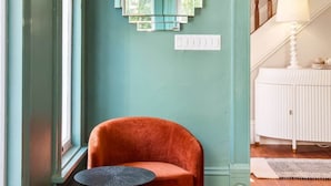 Una habitación con paredes color turquesa, una escalera de madera, un radiador blanco y una silla roja con una pequeña mesa.
