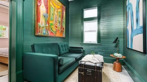 Una habitación con un sofá color turquesa, una maleta antigua y un cuadro abstracto y colorido en la pared.
