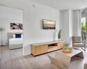 Una habitación de hotel moderna con cama, televisor, balcón con vista a palmeras y una consola de madera.