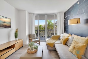 Una sala moderna con sofá, sillón, televisor, planta y balcón con vistas.
