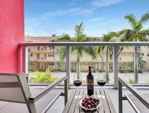 A balcony with a table, a bottle of wine, two glasses, and a plate of cherries. - Modern Resort:   Awesome Pool + Gym|Near Beach (Hallandale Beach)