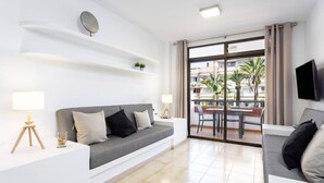 Una sala de estar moderna con un sofá gris, paredes blancas y un balcón con una mesa y sillas.