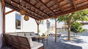 An outdoor patio area with a wooden bench, a table with fruit, and a covered seating area with a view of the building and palm trees. - Home2Book Stunning Design House Arafo (Arafo)