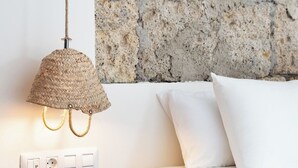A bedroom with a stone wall, a woven lamp, a bedside table, and a bed with white bedding. - Home2Book Stunning Design House Arafo (Arafo)