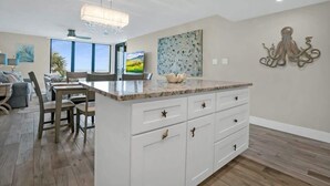 A spacious living area with a kitchen island, dining table, and chairs. There is a large window providing natural light and a view of the outdoors. - Oceanfront, Pool, Beach Gear, Tennis, Smart TVs (St. Augustine)