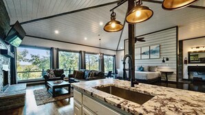 A spacious living area with a large kitchen island, a fireplace, and a dining area. - Treetop Views for Miles! New, Romantic Couples Cabin (Broken Bow)