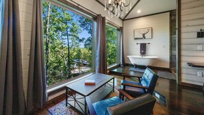 A modern interior with large windows, a chandelier, a dining area, and a bathroom. - Treetop Views for Miles! New, Romantic Couples Cabin (Broken Bow)
