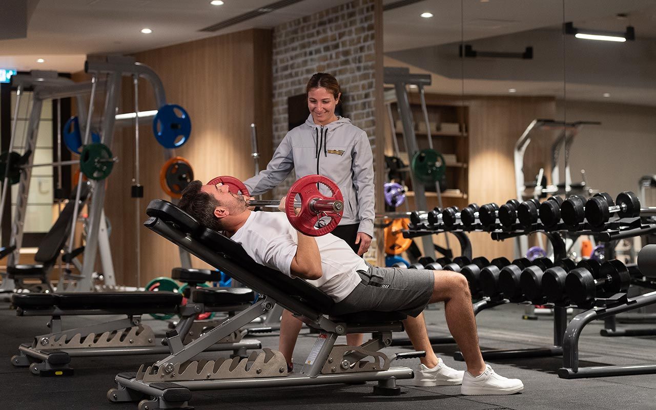 A gym with weightlifting equipment, a bench press, and a person performing a bench press exercise.