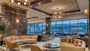 A spacious lobby with a sectional sofa, round coffee tables, and a large window offering a view of the outdoors.