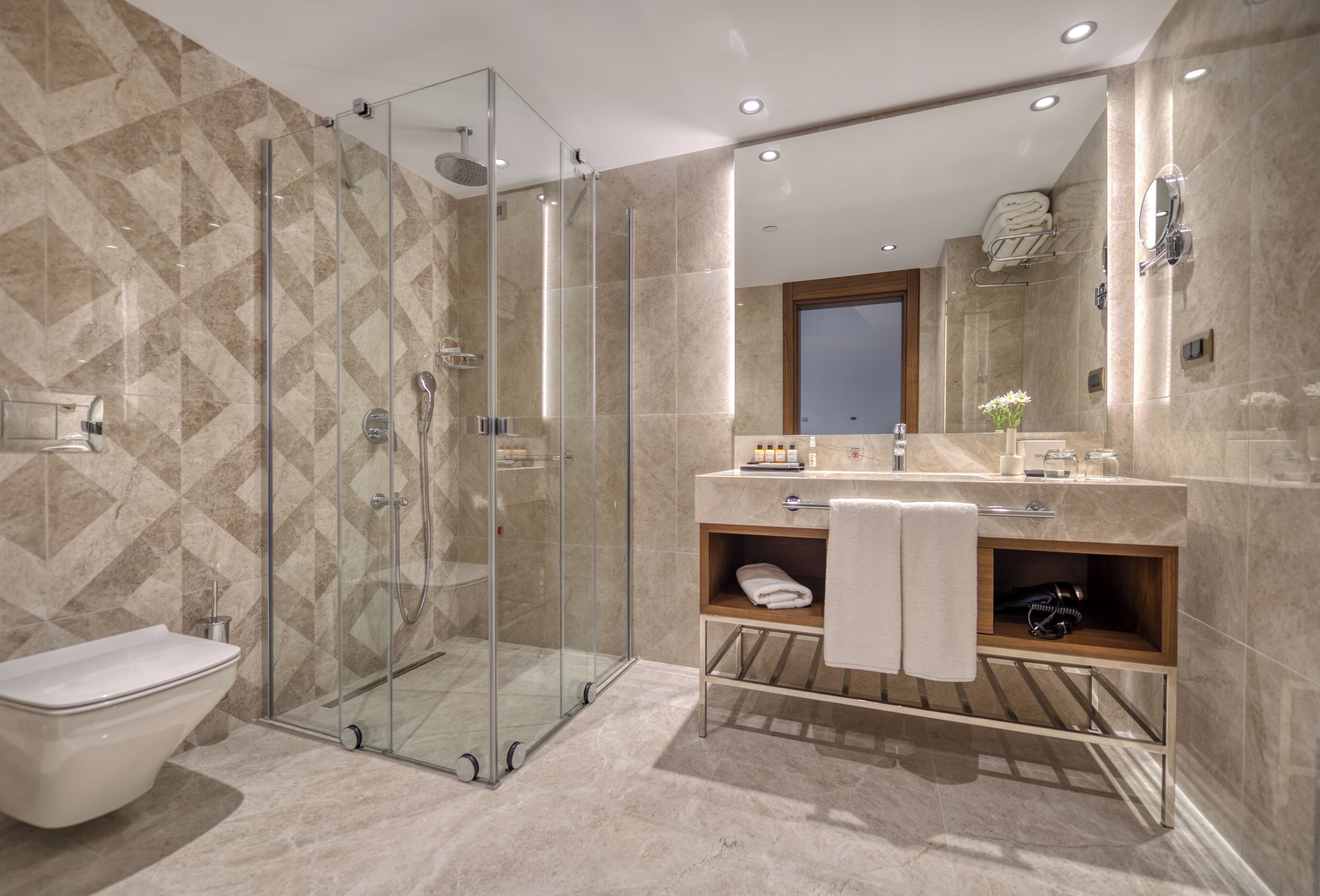 A modern bathroom with a glass-enclosed shower, a toilet, and a vanity with a mirror and towel rack.