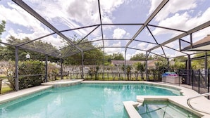 En pool med et overdækket område, omgivet af grønt og en blå himmel.