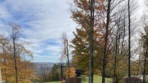 A wooden deck with a round table and chairs, overlooking a scenic view with trees and a distant landscape.