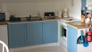 Une cuisine compacte avec des meubles bleus, un four à micro-ondes, une machine à café et un petit four.