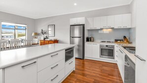 Una cocina moderna con armarios blancos, una isla grande, electrodomésticos de acero inoxidable y vistas al exterior.