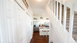Corredor com portas brancas, área de cozinha com geladeira, micro-ondas e banquetas de madeira.