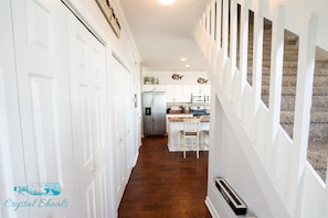 A hallway with white doors, a kitchen area with a refrigerator, microwave, and wooden bar stools. - Beachfront - Perfect for large groups - Pool! (Emerald Isle)