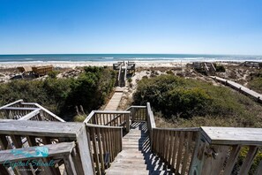 Una escalera de madera que lleva a sillas de playa y una terraza de madera con vistas al océano.