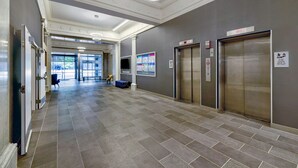 Un hall d’entrée spacieux avec un sol carrelé, deux ascenseurs et un coin salon doté d’un canapé bleu.