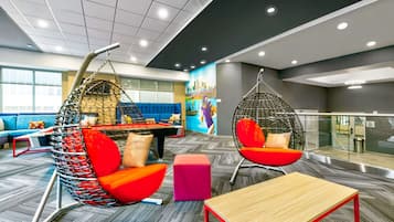 Un espacio de oficina moderno con una silla colgante, un asiento acolchado, una mesa de madera y un mural colorido en la pared.