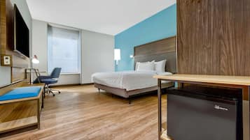 A hotel room with a bed, a desk, a chair, a TV, and a refrigerator.