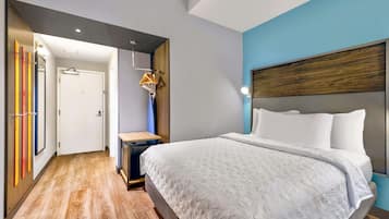 Una habitación de hotel moderna con una cama grande, cabecera de madera y una pared azul decorativa.