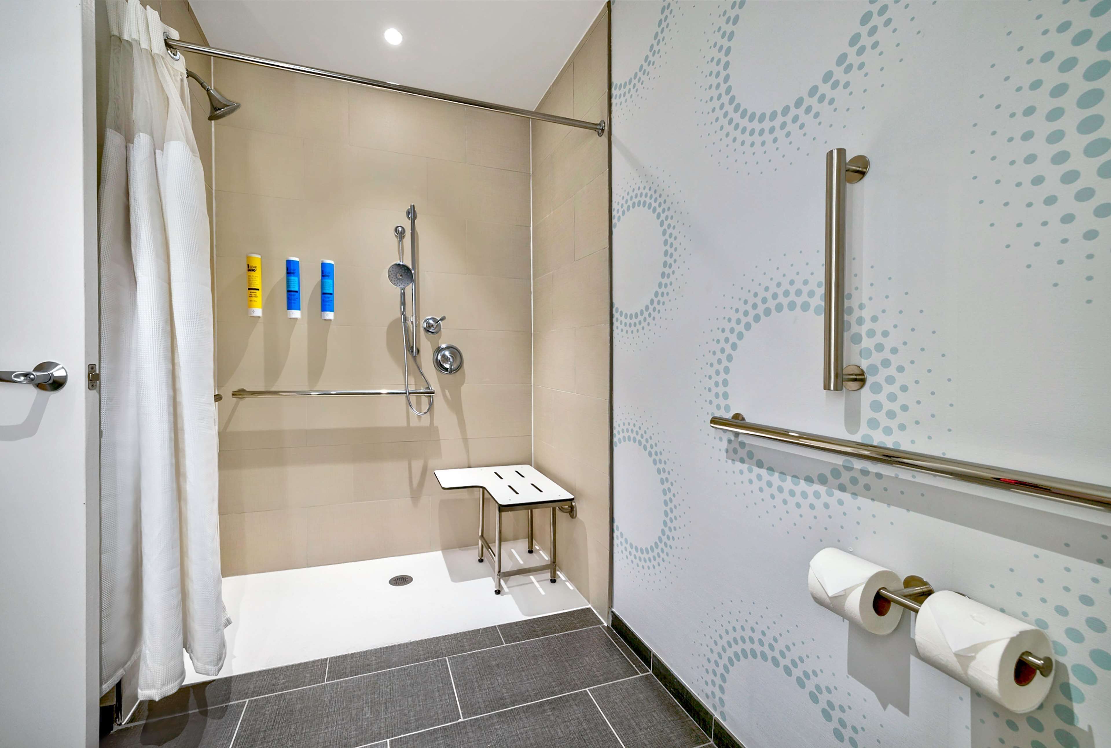 A modern bathroom with a shower, toilet paper, and toiletries.