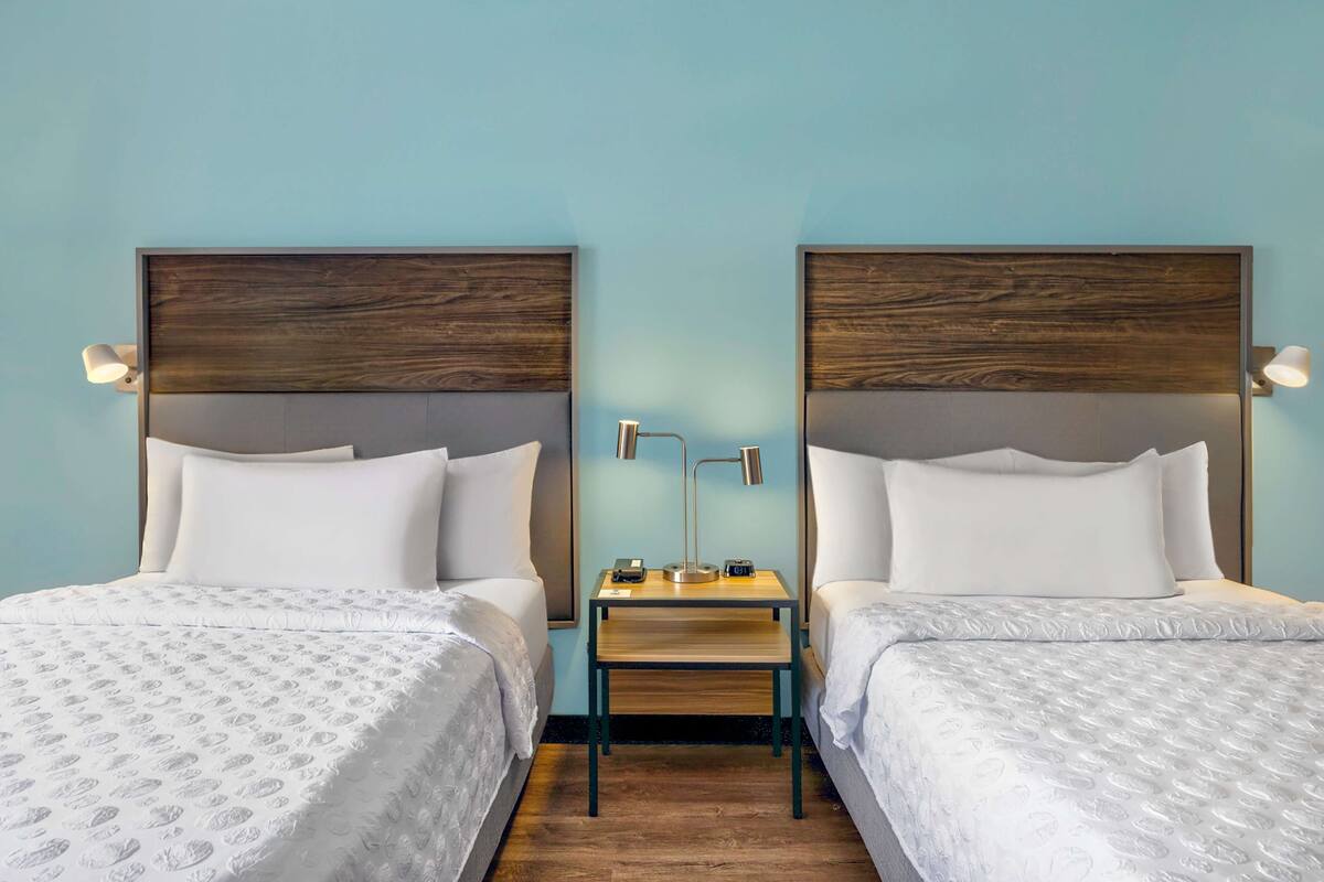 Habitación de hotel con dos camas, una mesita de noche y lámparas de noche.
