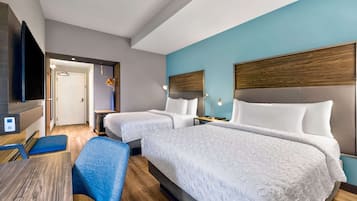 A hotel room with two beds, a desk, a chair, a TV, and a bathroom visible through an open door.