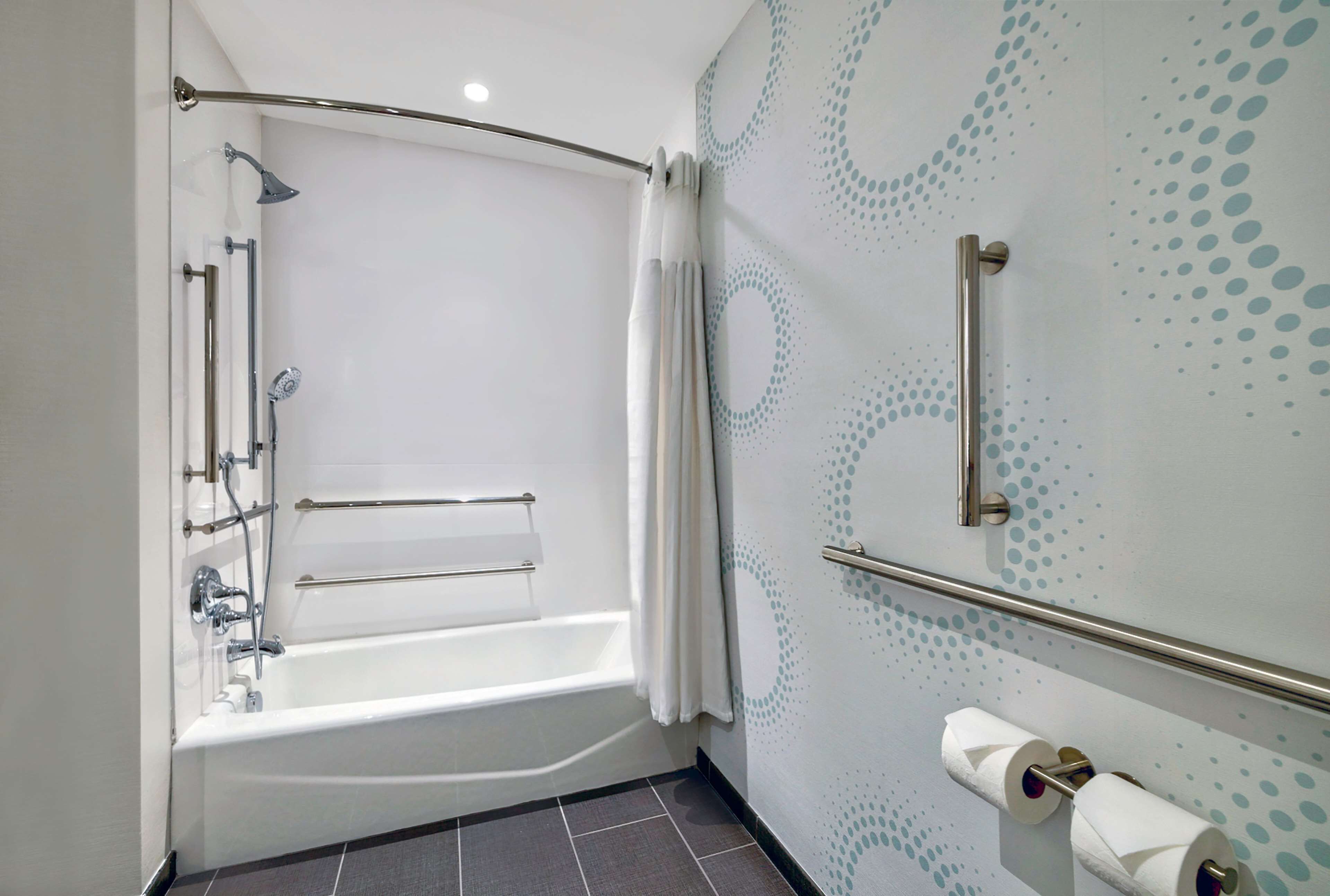 Un baño moderno con bañera, ducha y barras de apoyo.